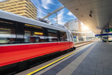 Red high speed train in motion on the railway station at sunset. Fast modern intercity train and blurred background. Railway platform. Railroad in Austria. Commercial and passenger transportation