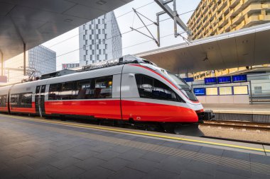 High speed train on the train station at sunset in Vienna, Austria. Beautiful red modern intercity passenger train on the railway platform and buildings. Railroad in Europe. Commercial transportation