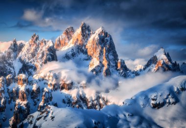Beautiful mountain peaks in snow in winter at sunrise. Colorful landscape with high snowy rocks in fog, blue sky with clouds in cold evening. Tre Cime in Dolomites, Italy. Alpine mountains. Nature
