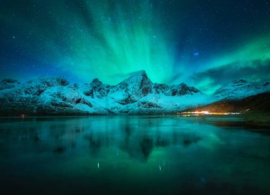 Karlı dağların üzerindeki kuzey ışıkları, donmuş deniz, gece vakti Lofoten, Norveç 'te sudaki yansıma. Aurora borealis ve karla kaplı kayalar. Kutup ışıkları, yıldızlı gökyüzü ve fiyortlu kış manzarası