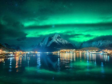 Reine, Lofoten Adaları, Norveç 'in kuzey ışıkları. Yıldızlı gökyüzü ve Aurora borealis, karlı dağlar, deniz kıyıları, evler, kayalar, sudaki yansıma, kış gecelerinde şehir ışıkları. Parlak kutup ışıkları