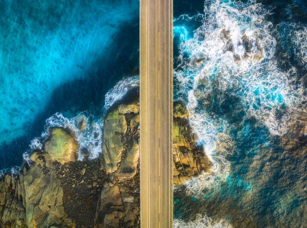 Aerial view of road, sea with waves and stones at sunset in Lofoten Islands, Norway. Landscape with beautiful bridge, transparent blue water, rocks. Top view from drone of highway in summer. Travel