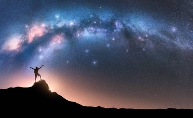 Milky Way and happy man with backpack on mountain peak at night. Silhouette of guy with raised up arm on the hill, sky with stars, yellow light in Nepal. Galaxy. Space landscape with milky way arch clipart