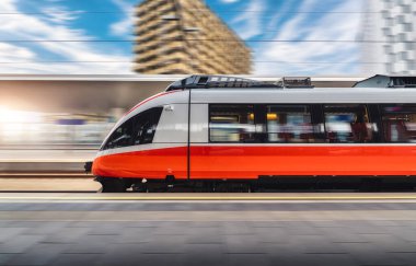 Kırmızı yüksek hızlı tren gün batımında tren istasyonunda hareket halinde. Hızlı modern şehirlerarası tren ve bulanık arka plan. Demiryolu platformu. Avusturya 'da demiryolu. Ticari ve yolcu taşımacılığı