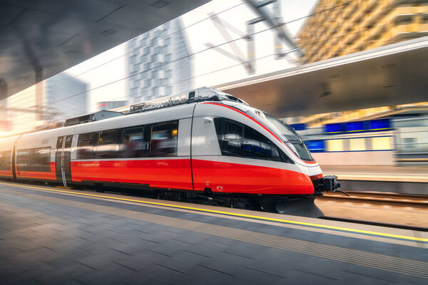 Red high speed train in motion on the railway station at sunset. Fast modern intercity train and blurred background. Railway platform. Railroad in Austria. Commercial and passenger transportation