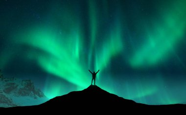 Kuzey ışıkları ve Norveç 'teki dağın zirvesinde kollarını kaldırmış ayakta duran adamın silueti. Aurora Borealis ve mutlu adam. Yıldızlı ve kutuplu gökyüzü. Aurora 'lı gece manzarası. Kavram