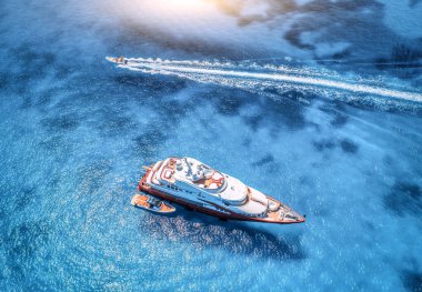 Yazın günbatımında mavi denizde güzel kırmızı lüks yat ve teknenin hava manzarası. Sardunya adası, İtalya. Hız teknesi, deniz kıyısı, şeffaf su. Seyahat et. Tropik bir manzara. Yat.