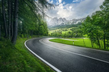 Yağmurlu yaz gününde yeşil ormanda yol. Dolomitler, İtalya. Güzel dağ yolu, kadın, çimen, yüksek kayalar, bulutlu mavi gökyüzü. Baharda ormanın içinden geçen boş otobanlı bir manzara. Seyahat