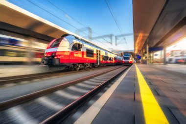 Turuncu yüksek hızlı tren gün batımında tren istasyonunda hareket halinde. Hızlı hareket eden modern şehirlerarası tren ve bulanık arka plan. Demiryolu platformu. Avusturya 'da demiryolu. Yolcu taşımacılığı. Kavram