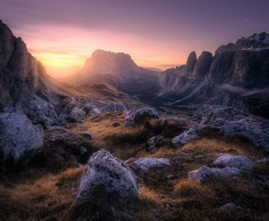 Dolomitler, İtalya 'da sonbaharda renkli günbatımında Dağ Vadisi. Kayalar, taşlar, patikalar, tepe, turuncu çimenler, geceleri bulutlu mor gökyüzü. Dağlarda yürüyüş. Alacakaranlık