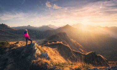 Dağın zirvesinde genç bir kadın ve sonbaharda renkli günbatımında sisli bir dağ vadisi. Dolomitler, İtalya. Sportif kız, sisli dağ tepeleri, turuncu çimenler, ağaçlar, sonbaharda altın güneş. Yürüyüş