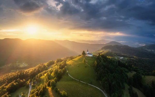在斯洛文尼亚 夏季日落时山顶上的小教堂的空中景观 山顶是美丽的小礼拜堂 小径环山 绿茵的草地 春天黄昏时的橙色天空 — 图库照片