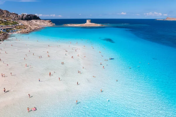 Aerial view of famous La Pelosa beach at sunny summer day. Stintino, Sardinia island, Italy. Top view of sandy beach, swimming people, clear blue sea, old tower and sky with clouds. Tropical seascape