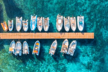 Aerial view of boats and luxure yachts in dock at sunset in summer in Sardinia, Italy. Colorful landscape with sailboats and motorboats in sea bay, jatty, clear blue sea. Top view of harbor. Travel