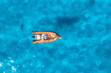 Yazın günbatımında mavi denizde güzel turuncu teknenin hava manzarası. Sardunya, İtalya. Motorlu teknenin üst drone görüntüsü, şeffaf gök mavisi suyu olan okyanus. Seyahat et. Tropik bir manzara. Yatçılık. Deniz Burnu