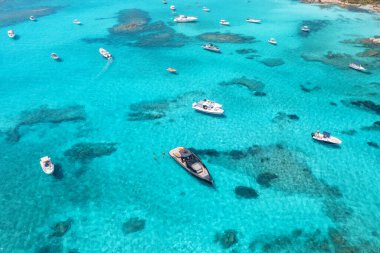 Yazın günbatımında mavi denizde lüks yatların ve teknelerin hava manzarası. Sardunya, İtalya 'ya seyahat. Motorlu teknelerden, yatlardan, deniz lagünlerinden şeffaf gök mavisi sularından insansız hava aracı görüntüsü. Deniz Burnu. Üst görünüm