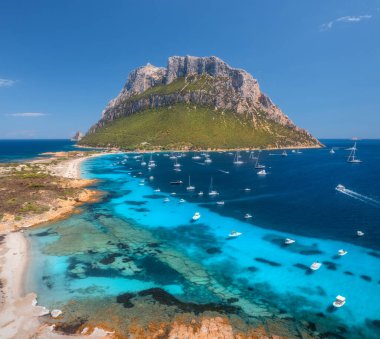 Lüks yatların ve mavi denizdeki teknelerin havadan görünüşü yaz güneşli günlerinde güzel bir dağ. Kumsal, kayalık deniz kıyısı, Sardinya, İtalya 'daki Tavolara adasında turkuaz su. Üst Manzara. Deniz Burnu