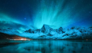 Karlı dağların üzerindeki kuzey ışıkları, donmuş deniz kıyıları, Norveç 'in Lofoten şehrinde kış gecelerinde suda yansıyan yansımalar. Aurora borealis ve karla kaplı kayalar. Doğa. Kutup ışıkları, yıldızlı gökyüzü ve fiyort