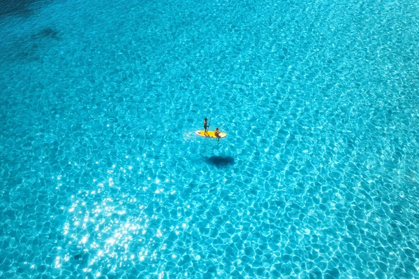夏の日没時に青い海の上にボード上の男性と女性との空中ビュー 透明水の中でカヌーの浮動小数点の人々 カヤック イタリアのサルデーニャ島 熱帯の海 アクティブな旅行 トップ表示 — ストック写真