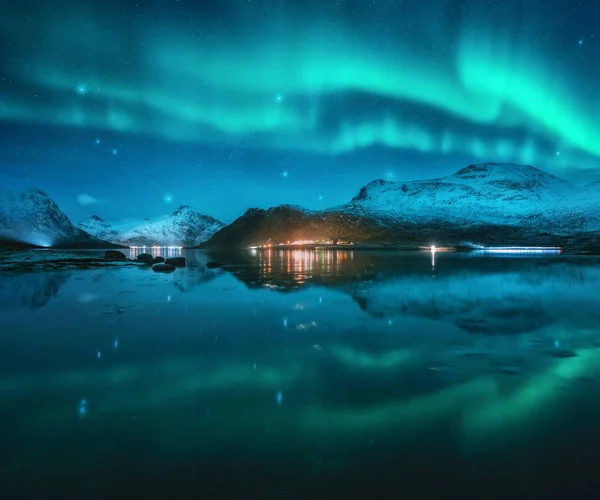 北极光笼罩着雪山 在冬日星夜倒映在水面上 挪威Lofoten 北极光和积雪覆盖了岩石 有极光 城市灯光 天空的风景 — 图库照片