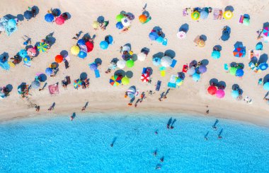 Kumlu sahildeki renkli şemsiyeler, güneşli yaz günlerinde mavi denizde yüzen insanlar. İtalya, Sardinya 'da bir tatil köyü. Turkuaz suyu olan tropik deniz manzarası. Seyahat ve tatil. Üst görünüm