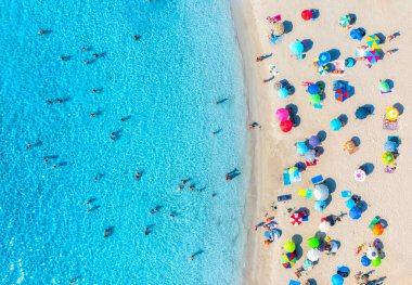 Kumlu sahildeki renkli şemsiyeler, güneşli yaz günlerinde mavi denizde yüzen insanlar. İtalya, Sardinya 'da bir tatil köyü. Turkuaz suyu olan tropik deniz manzarası. Seyahat ve tatil. Üst görünüm
