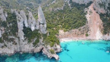 Kayaların ve dağların havadan görünüşü, deniz körfezi, sahil, yaz günü tekneler. Cala Goloritze, Sardunya Adası, İtalya. Uçurumların, taşların, yeşil ağaçların, gün batımında şeffaf masmavi suyun en üst drone görüntüsü