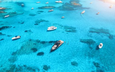 Yazın gündoğumunda mavi denizde lüks yatların ve teknelerin hava manzarası. Sardunya, İtalya 'ya seyahat. Motorlu teknelerden, yatlardan, deniz lagünlerinden şeffaf gök mavisi sularından insansız hava aracı görüntüsü. Deniz Burnu. Üst görünüm