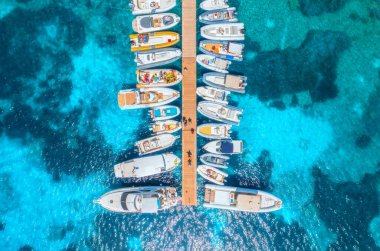 Aerial view of boats and luxure yachts in dock at sunset in summer in Sardinia, Italy. Colorful landscape with sailboats and motorboats in sea bay, jatty, clear blue sea. Top view of harbor. Travel