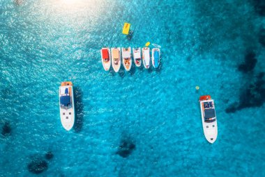 Yazın gündoğumunda mavi denizde lüks yatların ve teknelerin hava manzarası. Sardunya, İtalya 'ya seyahat. Motorlu teknelerden, yatlardan, deniz lagünlerinden şeffaf gök mavisi sularından insansız hava aracı görüntüsü. Deniz Burnu. Üst görünüm