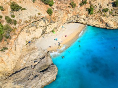Yazın güneşli bir günde yaban sahili, mavi deniz, kaya, şemsiye manzarası. Oludeniz, Türkiye 'de tatil. Deniz kıyısının güzel manzarası, yüzen insanlar, gök mavisi su. Üst dron görüntüsü. Seyahat