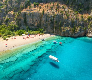Kumlu sahil manzarası, mavi deniz, yat ve tekne, kayalar, şemsiyeler yaz güneşli günlerinde. Oludeniz, Türkiye 'deki Kelebek Vadisi. Deniz kıyısının en iyi insansız hava aracı görüntüsü, yüzen insanlar, temiz gök mavisi suyu. Seyahat