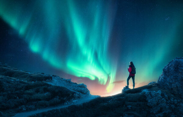 Northern lights and woman on mountain peak at night. Aurora borealis and silhouette of alone girl on mountain trail. Landscape with polar lights. Sky with stars and bright aurora. Travel background