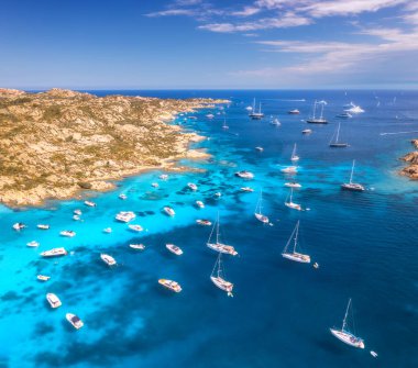 Güneşli bir yaz gününde deniz koyundaki lüks yatların ve teknelerin hava manzarası. Sardunya, İtalya 'ya seyahat. Sürat tekneleri, yatlar, deniz lagünleri, kayalık kıyılar, şeffaf su. Üst görünüm