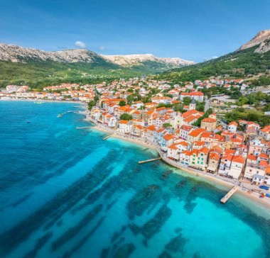 Turuncu çatısı, kumsalı, dağları, yaz günü mavi denizi olan binaların hava manzarası. Hırvatistan 'ın Krk adasındaki güzel Baska şehrinde tatil. Evlerin, sokakların, gezinti alanlarının, Adriyatik Körfezi 'nin en üst manzarası