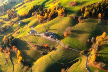 Muhteşem yeşil çayırların, tepelerdeki portakal ağaçlarının, sonbaharda günbatımında dağ köyündeki binaların havadan görünüşü. Santa Magdalena, Dolomitler, İtalya. Sonbaharda ev, yol, orman manzarası