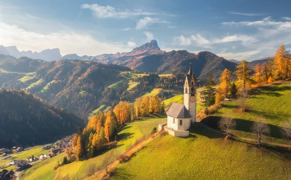 Güzel kilise manzarası, yeşil alp çayırları, portakal ağaçları, sonbaharda gün batımında dağ köyündeki tepeler. Dolomitler, İtalya. Eski şapelin üst manzarası, kayalar, orman, sonbaharda bulutlu gökyüzü