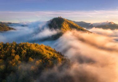 Sonbaharda gündoğumunda alçak bulutlarda dağ zirvesinin havadan görünüşü. Siste kırmızı ve turuncu ağaçlı tepelerin, sonbaharda renkli gökyüzünün en üst drone görüntüsü. Slovenya. Doğa. Dağ vadisi. Sonbahar ormanı. Alpler