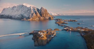 Karlı kayaların hava manzarası, deniz, köprü, dağlar, yol, kışın güneş doğarken bulutlu bulutlu adalar. Norveç, Lofoten Adaları 'ndaki Hamnoy köyünün güzel insansız hava aracı manzarası.