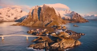 Karlı kayaların havadan görünüşü, deniz, köprü, dağlar, yol, kışın pembe gündoğumunda bulutlu adalar. Norveç, Lofoten Adaları 'ndaki Hamnoy köyünün güzel insansız hava aracı manzarası.
