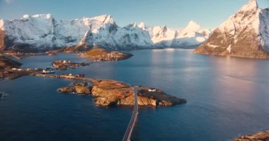 Kardaki kayaların havadan görünüşü, deniz, köprü, dağlar, yol, kışın gündoğumunda mavi gökyüzü olan adalar. Norveç, Lofoten Adaları 'ndaki Hamnoy ve Reine köyünün güzel insansız hava aracı manzarası. Seyahat