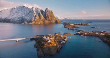 Karlı kayaların havadan görünüşü, deniz, köprü, dağlar, yol, rorbu, kışın renkli gündoğumunda bulutlarla kaplı adalar. Norveç, Lofoten adalarındaki Hamnoy köyünün inanılmaz insansız hava aracı görüntüsü