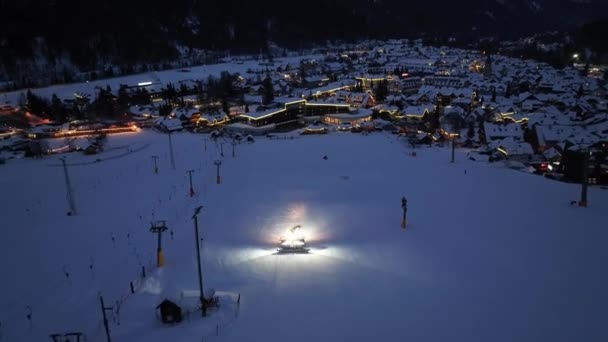 スロベニアのクルンダラ村で冬の夜に雪の高いアルプスキー場で働くスノーキャットの空中ビュー 雪が降るスノーキャットのトップドローンビュー スキーリゾート 夕暮れの街灯 スノープラウ — ストック動画
