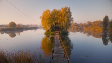 Sonbaharda gündoğumunda eski balıkçı evi ve ahşap rıhtımın havadan görünüşü. Gölde küçük bir adada evi olan güzel bir manzara, portakal ağaçları, iskele, suda yansıması. Ukrayna 'da düşmek. Üst görünüm