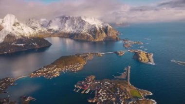 Karlı kayaların havadan görünüşü, gölgelikli adalar, deniz koyları, dağlar, yol, kışın alçak bulutlu pembe gökyüzü. Norveç, Lofoten Adaları 'ndaki Reine köyünün güzel insansız hava aracı manzarası