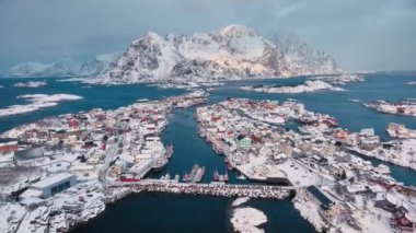 Norveç 'in Lofoten Adaları' ndaki Henningsvaer balıkçı köyünün kışın gün batımında hava manzarası. Kardaki, denizdeki, teknelerdeki, köprüdeki, yoldaki, bulutlu gökyüzündeki, kasabadaki, terör örgütündeki ve evlerdeki yüksek drone manzarası