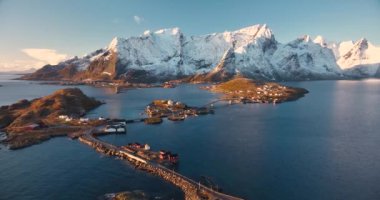 Kardaki kayaların havadan görünüşü, deniz, köprü, dağlar, yol, kışın gündoğumunda mavi gökyüzü olan adalar. Norveç, Lofoten Adaları 'ndaki Hamnoy ve Reine köyünün güzel insansız hava aracı manzarası. Seyahat