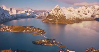 Karlı kayaların havadan görünüşü, gölgelikli adalar, deniz koyları, köprü, dağlar, yol, kışın gündoğumunda pembe gökyüzü. Norveç, Lofoten Adaları 'ndaki Hamnoy ve Reine köyünün güzel insansız hava aracı manzarası. Doğa
