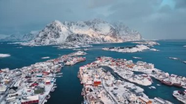 Norveç 'in Lofoten Adaları' ndaki Henningsvaer balıkçı köyünün kışın gün batımında hava manzarası. Kardaki, denizdeki, teknelerdeki, köprüdeki, yoldaki, bulutlu gökyüzündeki, kasabadaki, terör örgütündeki ve evlerdeki yüksek drone manzarası