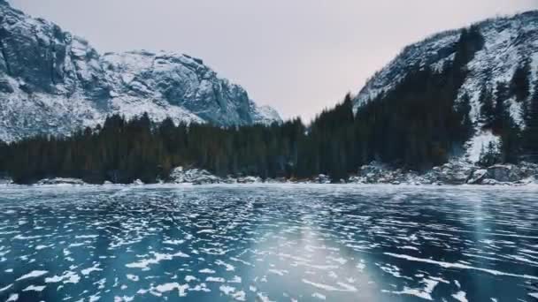 冬の雪山での凍った湖の低空飛行ドローンからの空中視界 ノルウェーのロフテン諸島 凍った川のトップビュー 氷の反射 雪の岩 曇った天気 ネイチャー — ストック動画